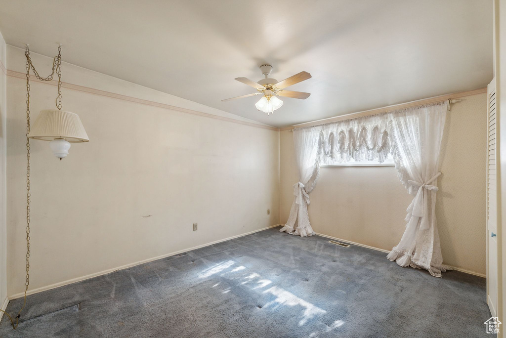 Empty room featuring ceiling fan and dark colored carpet