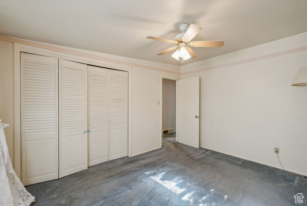 Unfurnished bedroom with dark colored carpet, a closet, and ceiling fan