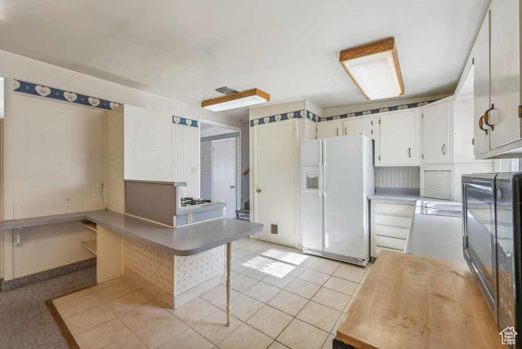 Kitchen featuring white cabinetry, white refrigerator with ice dispenser, and light tile patterned floors