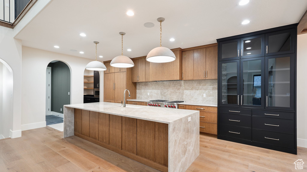 Kitchen with light hardwood / wood-style floors, light stone countertops, hanging light fixtures, and a center island with sink