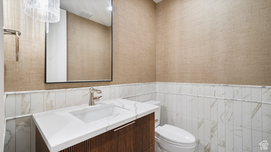 Bathroom featuring vanity, toilet, tile walls, and an inviting chandelier