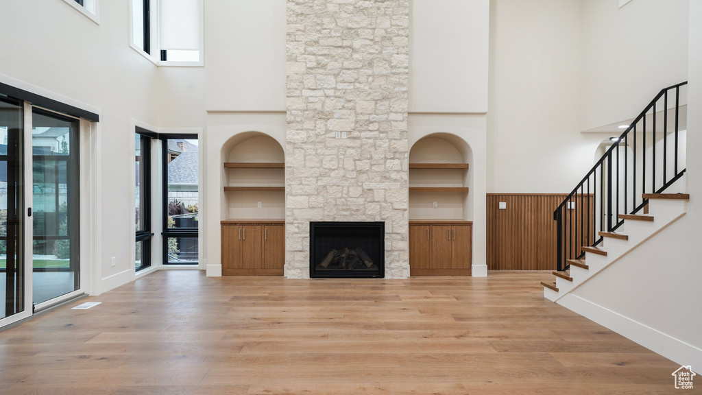 Unfurnished living room with hardwood / wood-style flooring, a high ceiling, a stone fireplace, and built in shelves