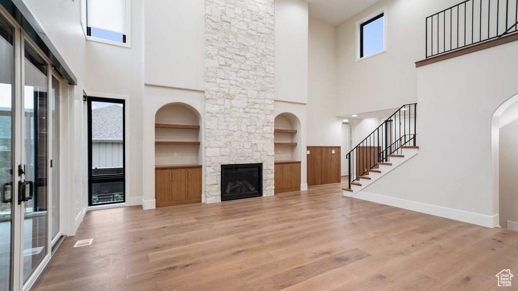 Living room with light hardwood / wood-style floors, a stone fireplace, built in features, and a high ceiling