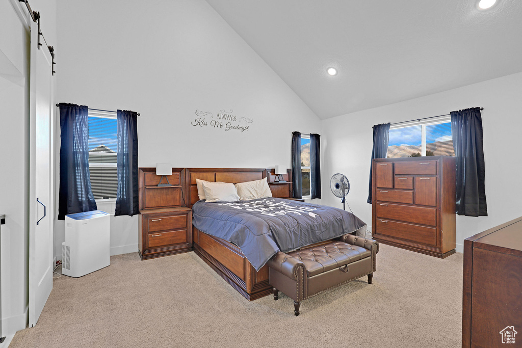 Bedroom featuring a barn door, light carpet, and high vaulted ceiling