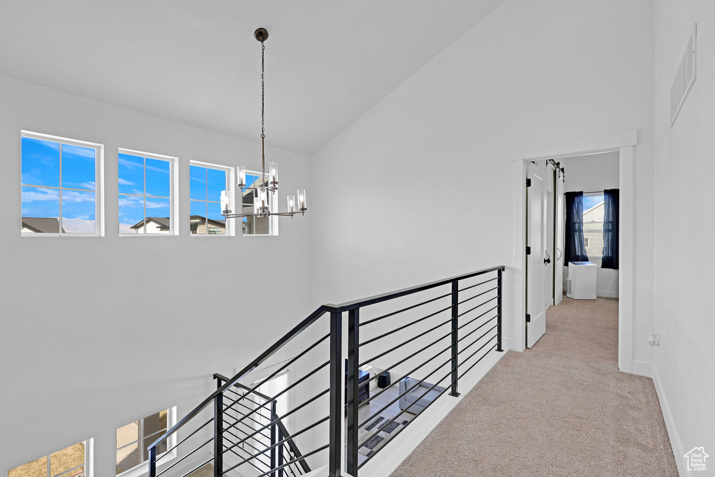 Hallway with light carpet, a notable chandelier, and high vaulted ceiling