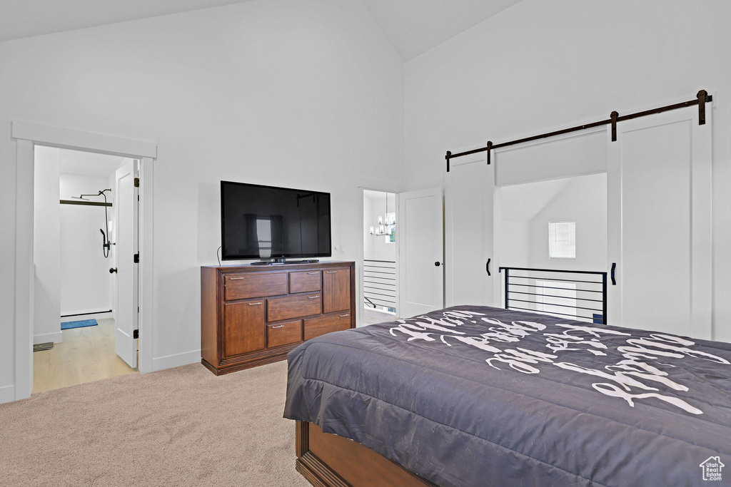 Bedroom featuring connected bathroom, high vaulted ceiling, light colored carpet, and a barn door