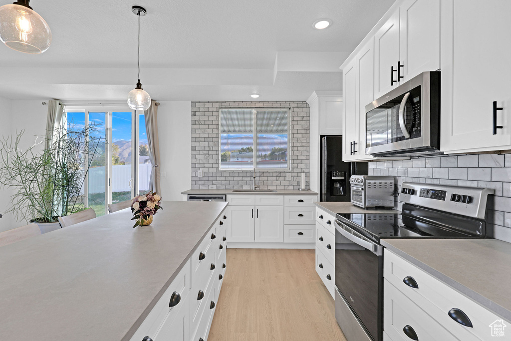 Kitchen with white cabinetry, stainless steel appliances, backsplash, and pendant lighting