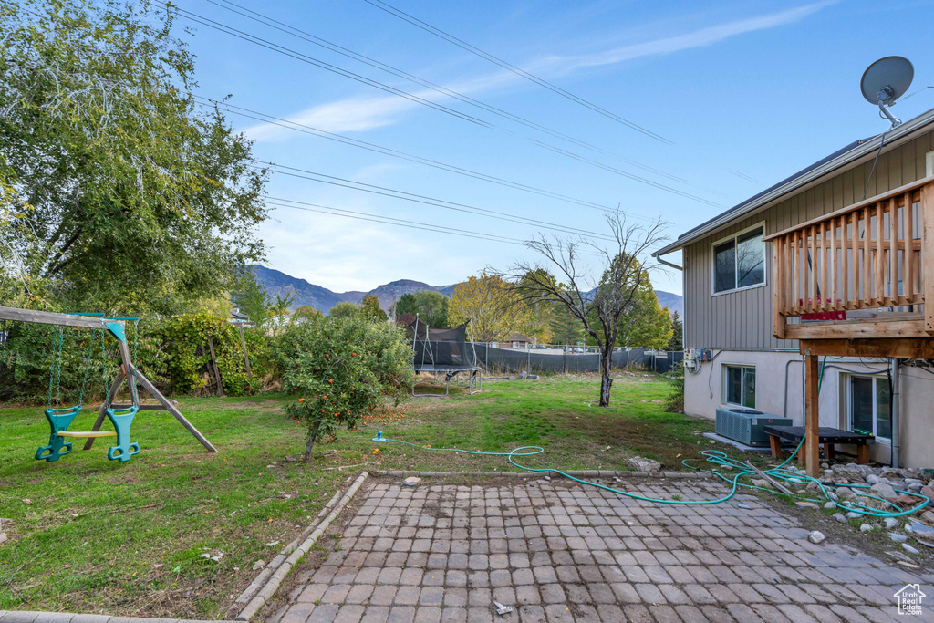 View of yard with central air condition unit, a playground, a mountain view, a trampoline, and a patio