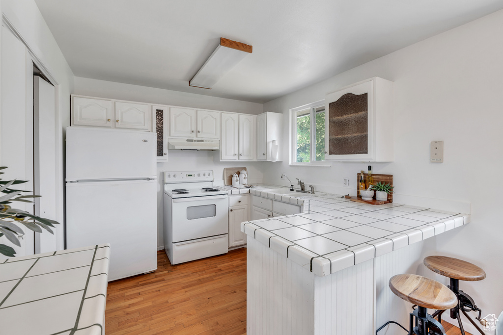 Kitchen featuring kitchen peninsula, white cabinetry, light wood-type flooring, tile counters, and white appliances