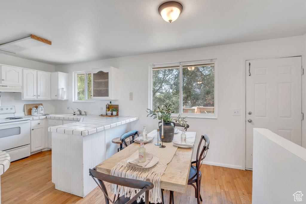 Kitchen featuring exhaust hood, white cabinets, light hardwood / wood-style flooring, and white electric stove