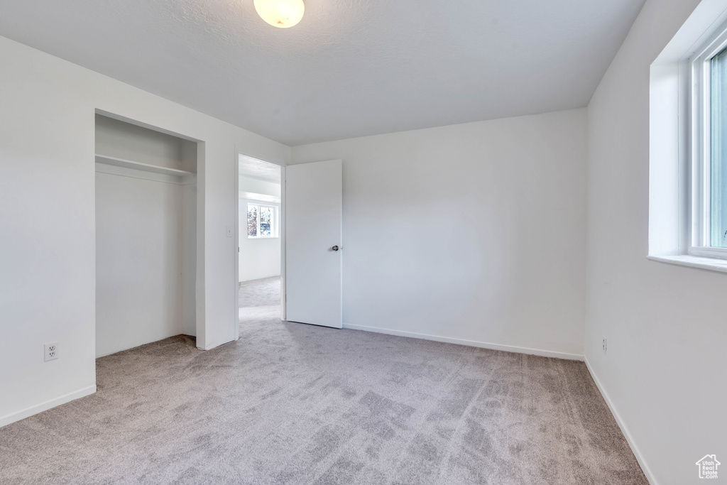 Unfurnished bedroom featuring multiple windows, a closet, and light colored carpet