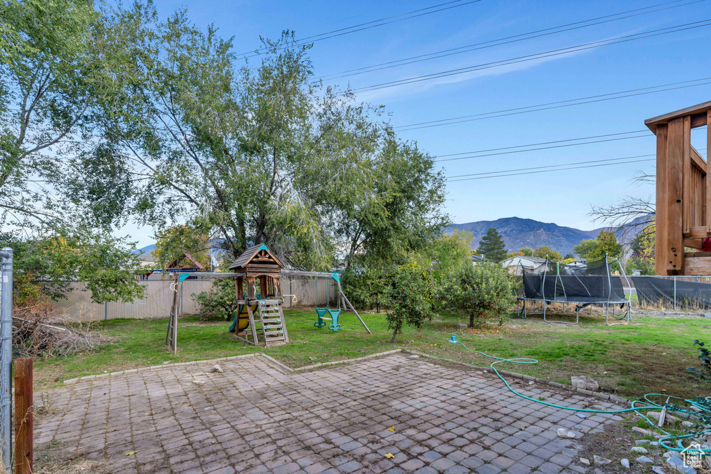 View of patio with a mountain view, a playground, and a trampoline