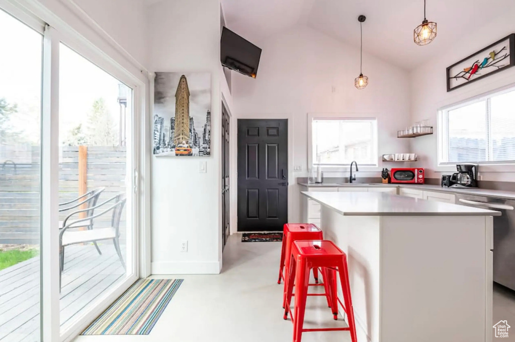 Kitchen featuring lofted ceiling, a breakfast bar, white cabinetry, decorative light fixtures, and a center island