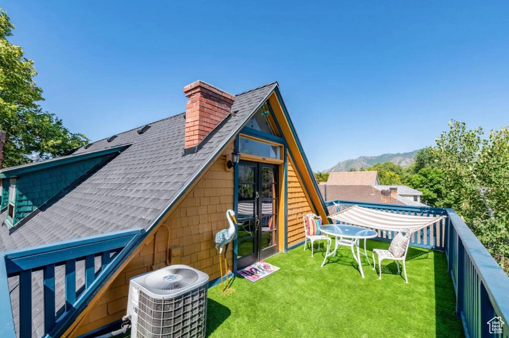 Back of property with a yard, a mountain view, and central AC unit