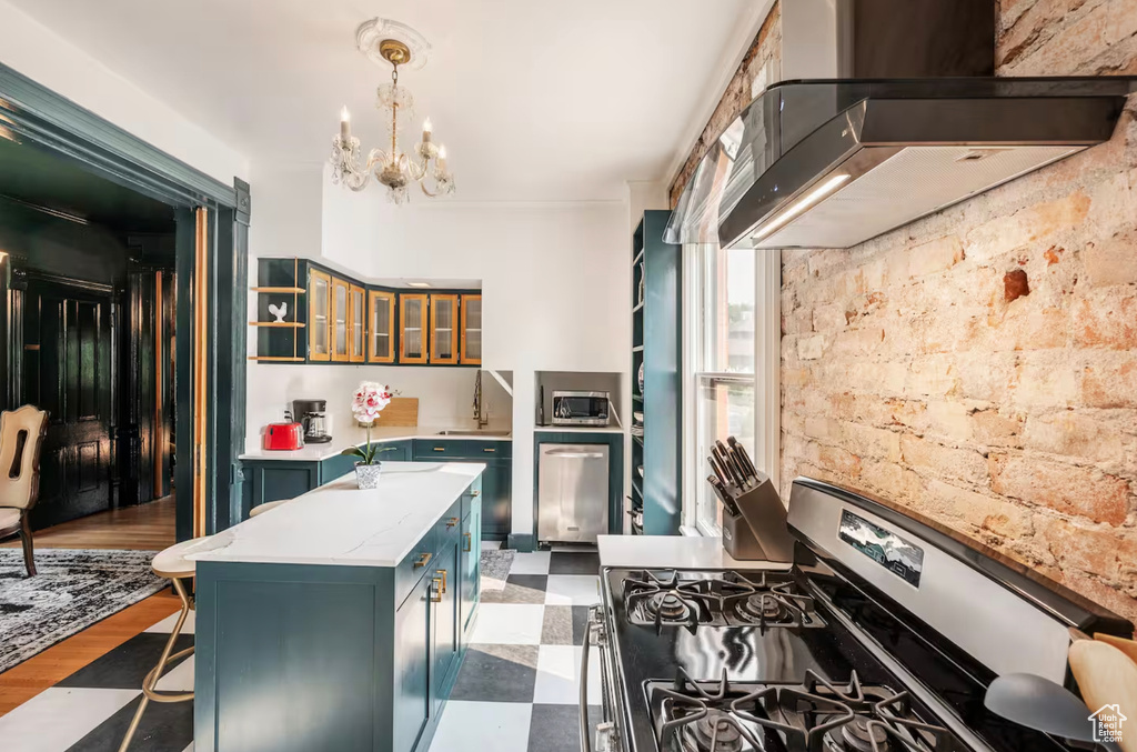 Kitchen with wall chimney range hood, dark hardwood / wood-style floors, stainless steel appliances, a notable chandelier, and decorative light fixtures