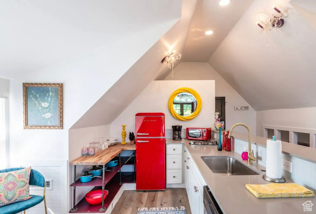 Kitchen with lofted ceiling, white cabinets, light hardwood / wood-style flooring, dishwasher, and sink