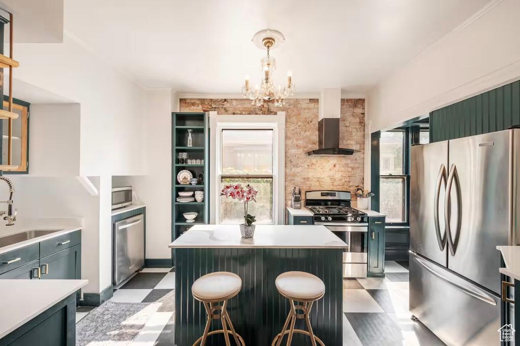 Kitchen with wall chimney range hood, stainless steel appliances, sink, a center island, and decorative light fixtures