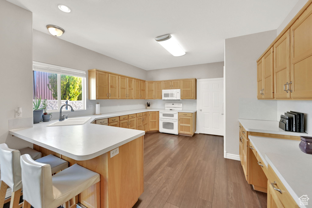 Kitchen with white appliances, sink, dark hardwood / wood-style flooring, kitchen peninsula, and a breakfast bar