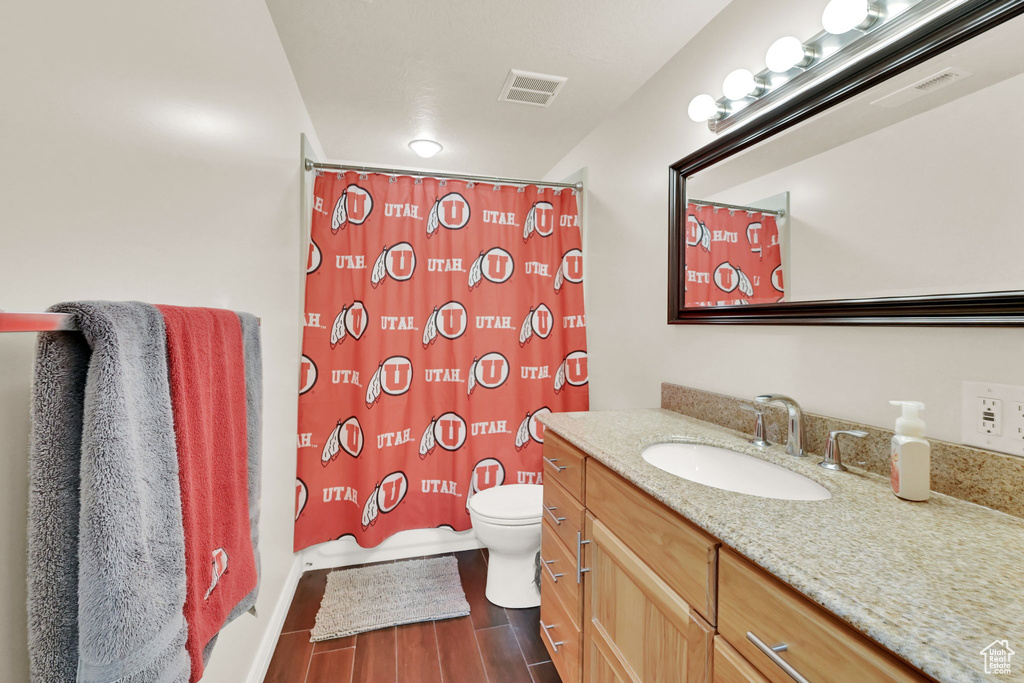 Full bathroom featuring vanity, hardwood / wood-style floors, shower / bath combo with shower curtain, and toilet