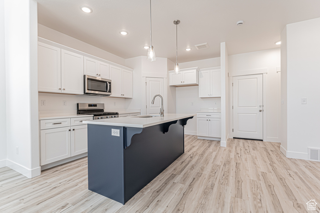 Kitchen with appliances with stainless steel finishes, white cabinetry, light wood-style flooring, an island with sink, and recessed lighting