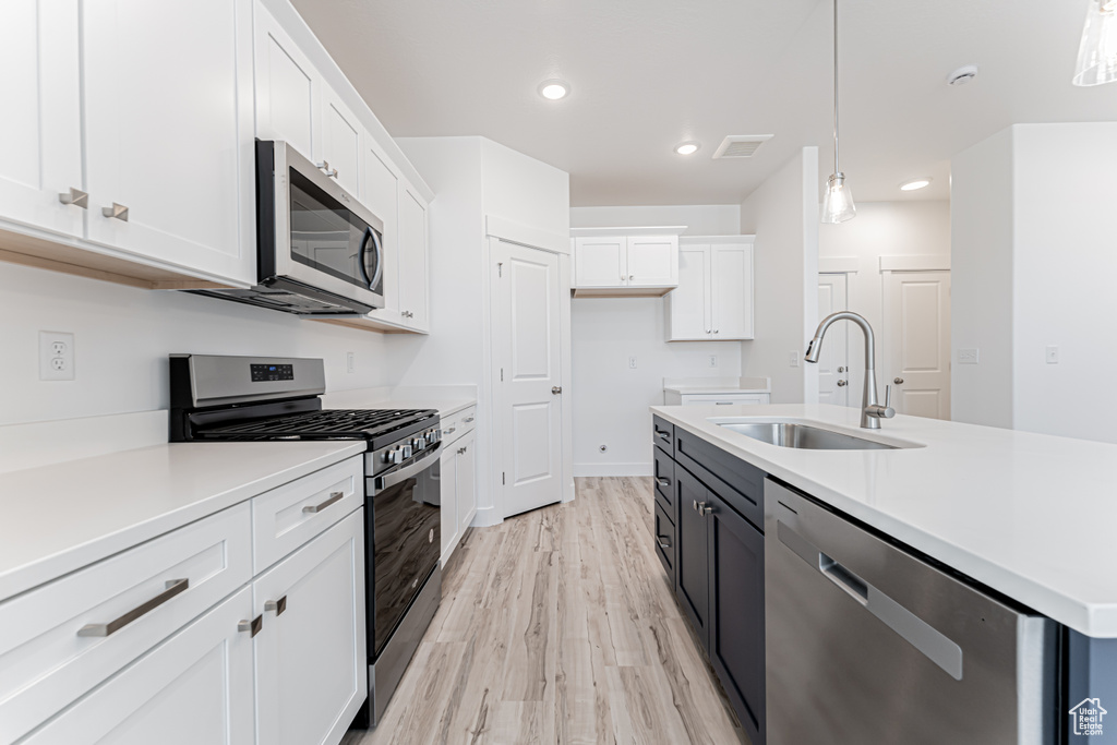 Kitchen featuring appliances with stainless steel finishes, white cabinets, light countertops, light wood finished floors, and recessed lighting