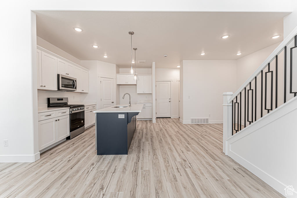 Kitchen with stainless steel appliances, white cabinetry, light wood-style floors, an island with sink, and light countertops