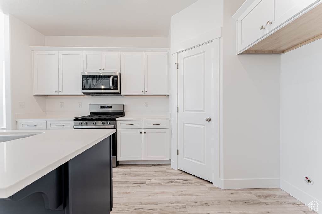 Kitchen with appliances with stainless steel finishes, light countertops, light wood-type flooring, and white cabinetry