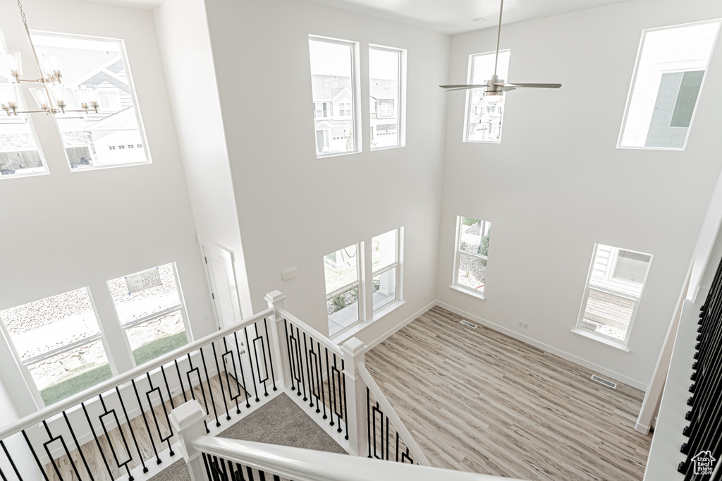 Staircase with a towering ceiling, a chandelier, wood finished floors, and a ceiling fan