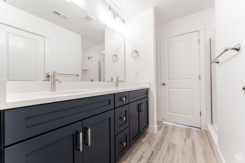 Bathroom with double vanity, wood finished floors, and a shower