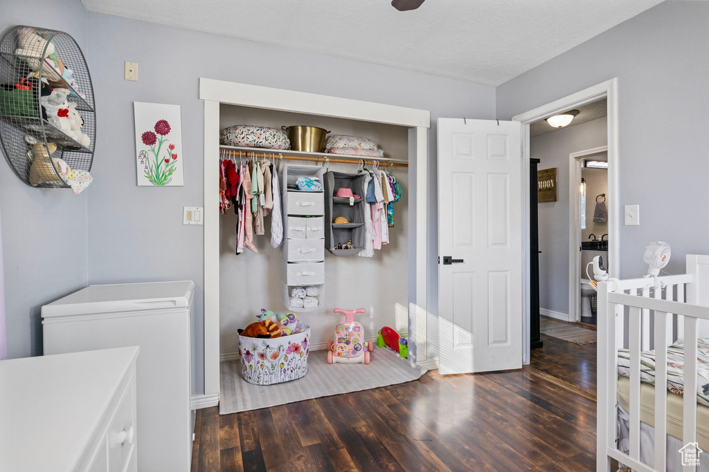 Bedroom featuring a nursery area, a textured ceiling, a closet, and dark hardwood / wood-style flooring