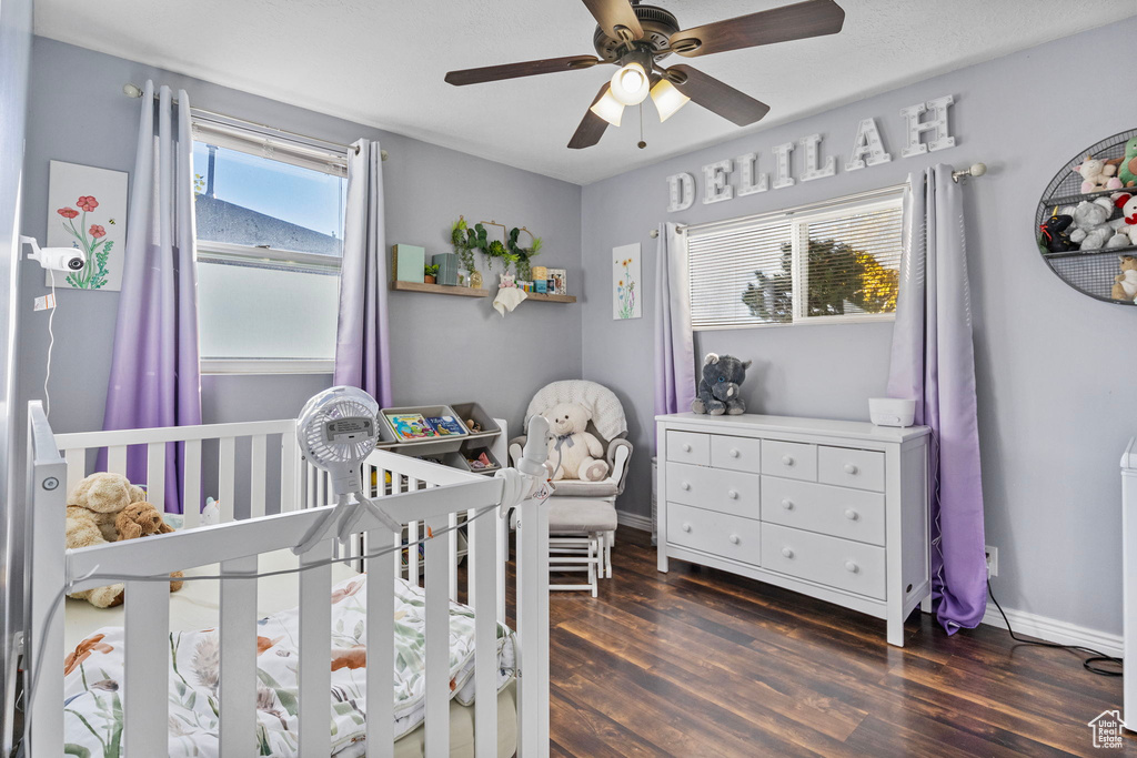 Bedroom with a nursery area, dark hardwood / wood-style floors, and ceiling fan