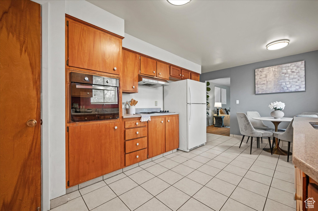 Kitchen with oven, light tile patterned flooring, and white refrigerator