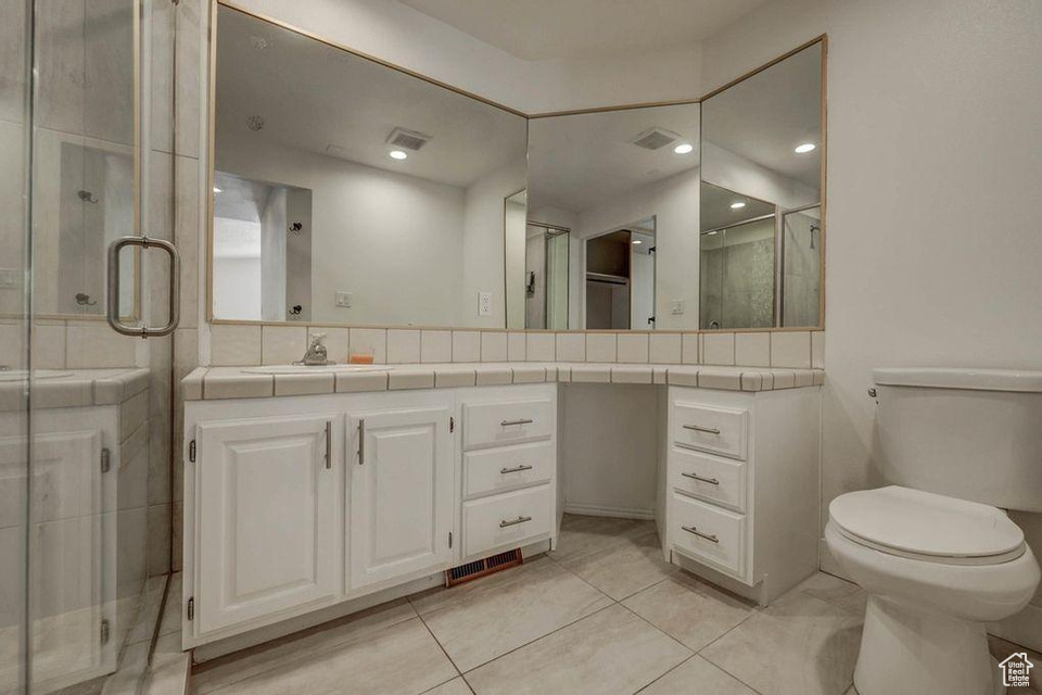 Bathroom featuring a shower with door, vanity, toilet, and tile patterned floors