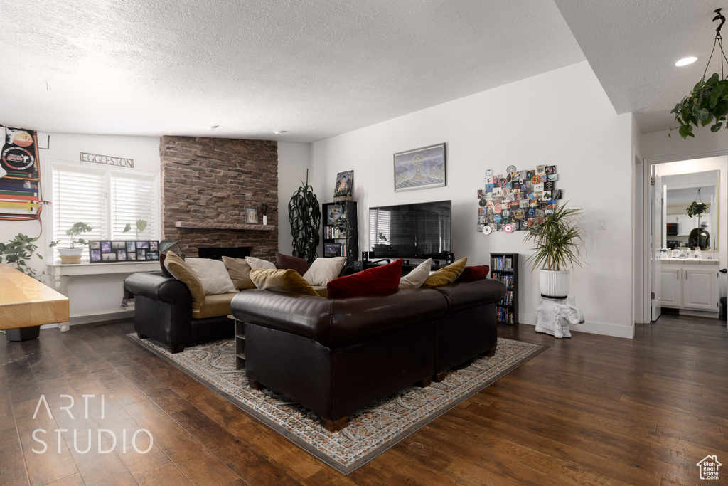 Living room featuring vaulted ceiling, a stone fireplace, a textured ceiling, and dark hardwood / wood-style flooring