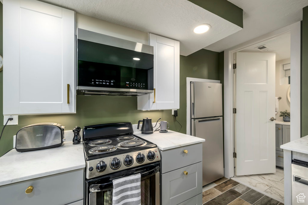 Kitchen with a textured ceiling, white cabinets, stainless steel appliances, and gray cabinetry