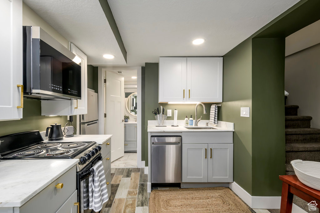 Kitchen with gray cabinetry, appliances with stainless steel finishes, sink, white cabinets, and light hardwood / wood-style flooring