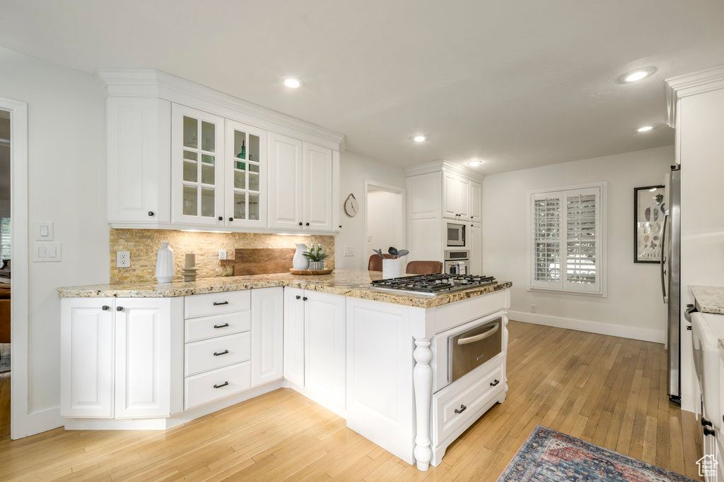 Kitchen featuring kitchen peninsula, tasteful backsplash, white cabinetry, light hardwood / wood-style flooring, and stainless steel appliances