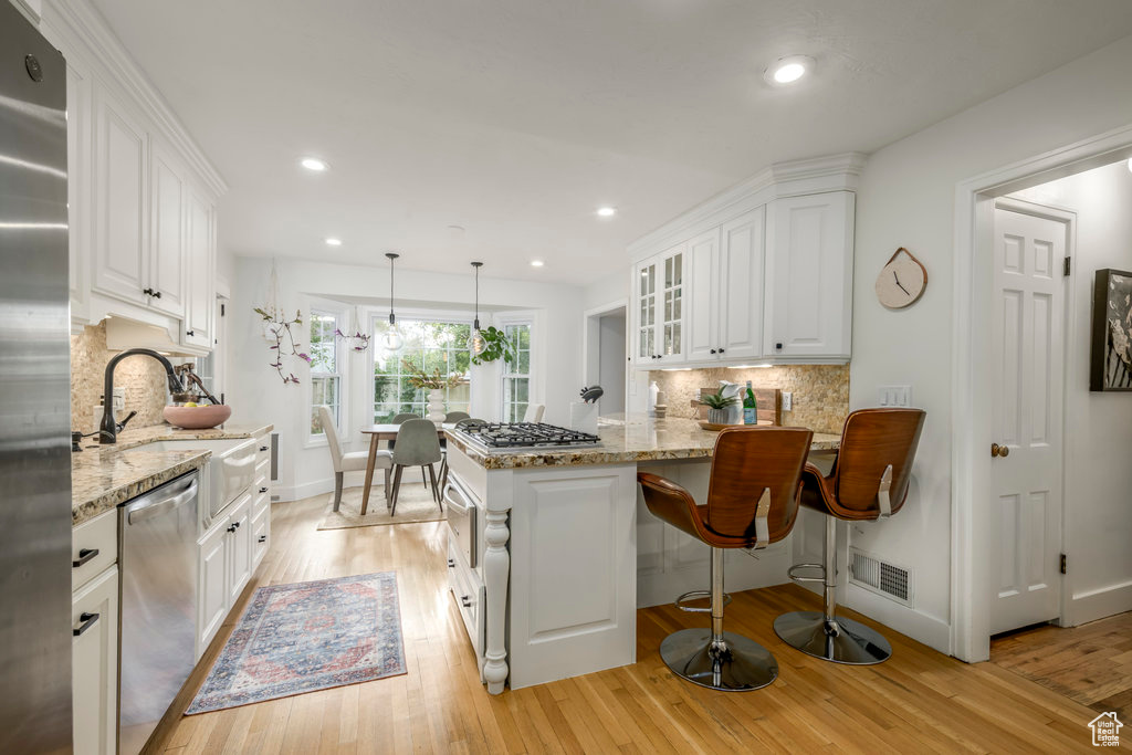 Kitchen with light hardwood / wood-style flooring, hanging light fixtures, backsplash, white cabinets, and appliances with stainless steel finishes