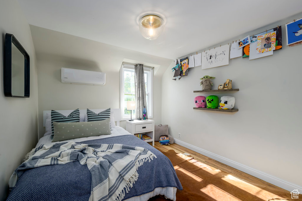 Bedroom with a wall mounted AC and wood-type flooring