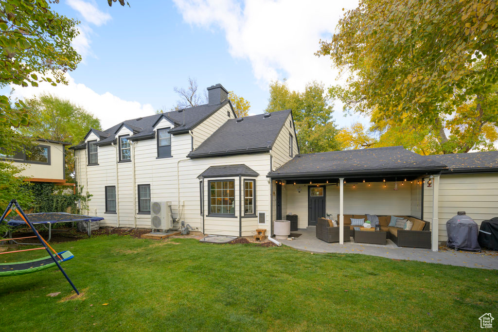 Back of property with a patio, a trampoline, ac unit, an outdoor living space, and a lawn