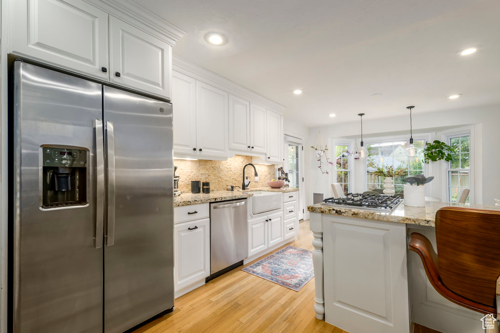 Kitchen with sink, light hardwood / wood-style floors, stainless steel appliances, pendant lighting, and white cabinets