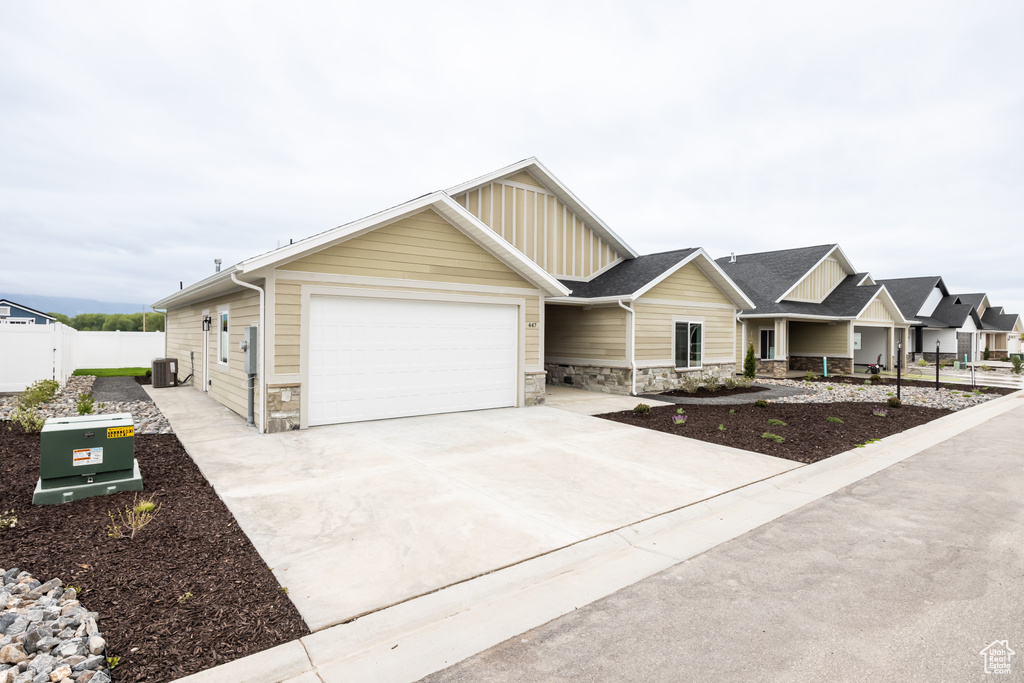 View of front facade with stone siding, board and batten siding, an attached garage, concrete driveway, and fence