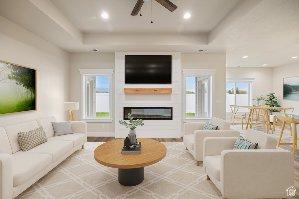 Living room with a large fireplace, wood finished floors, ceiling fan, baseboards, and a tray ceiling