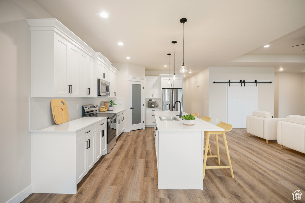 Kitchen featuring stainless steel appliances, a sink, recessed lighting, a breakfast bar area, and light wood finished floors