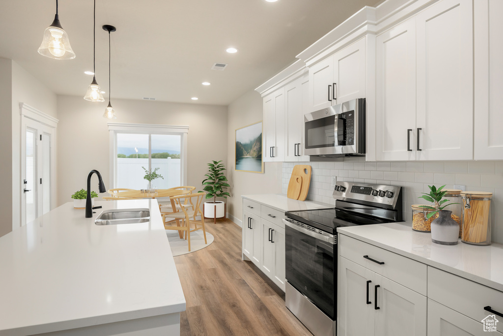 Kitchen with stainless steel appliances, a sink, decorative backsplash, recessed lighting, and light wood-style floors
