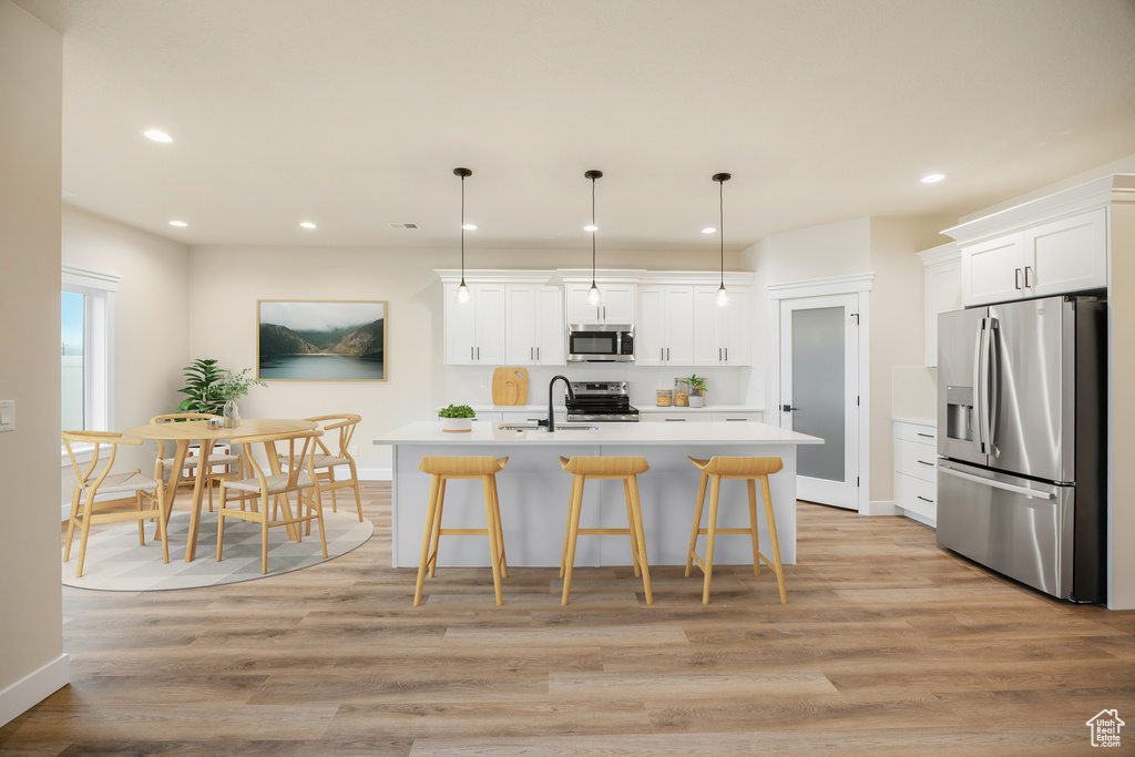 Kitchen with appliances with stainless steel finishes, a sink, light countertops, light wood-style floors, and white cabinets