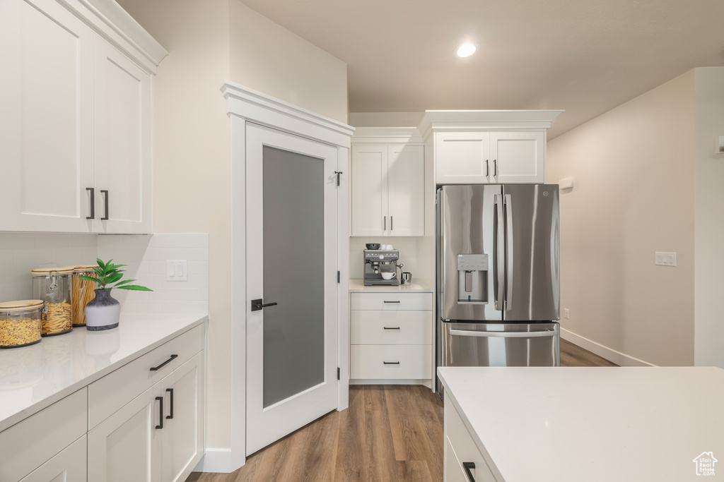 Kitchen with stainless steel fridge with ice dispenser, wood finished floors, light countertops, white cabinets, and recessed lighting