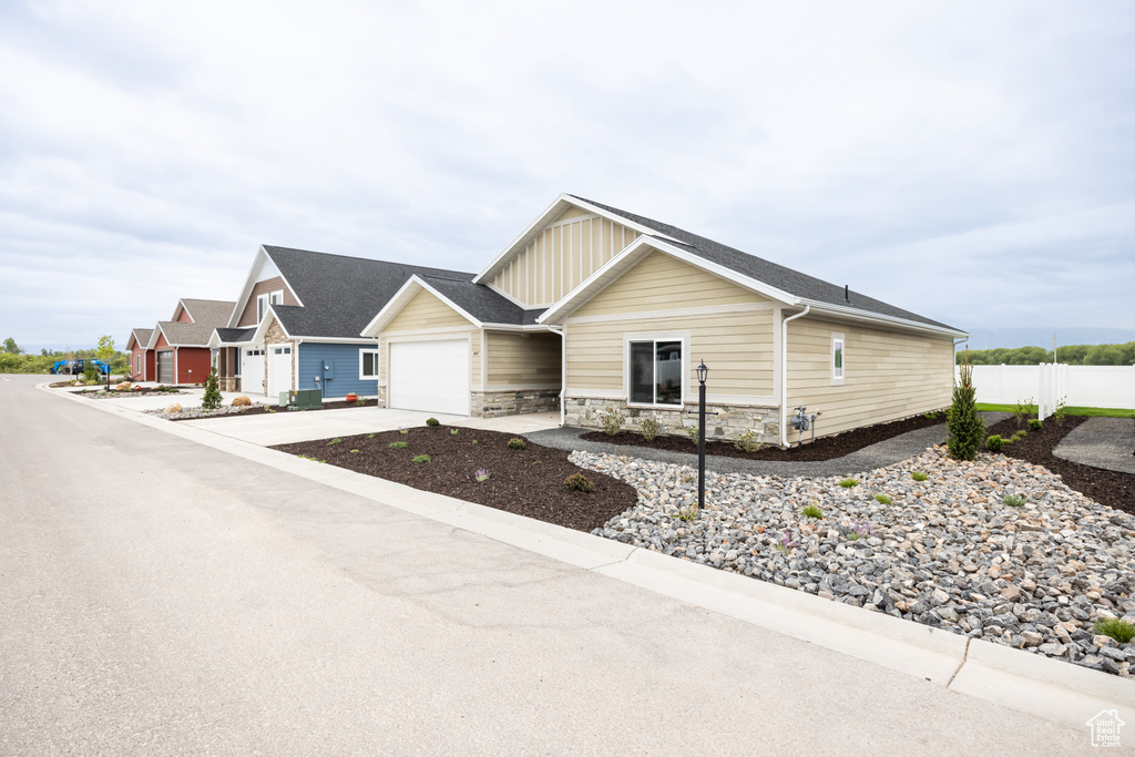 View of front facade with an attached garage, board and batten siding, driveway, fence, and stone siding