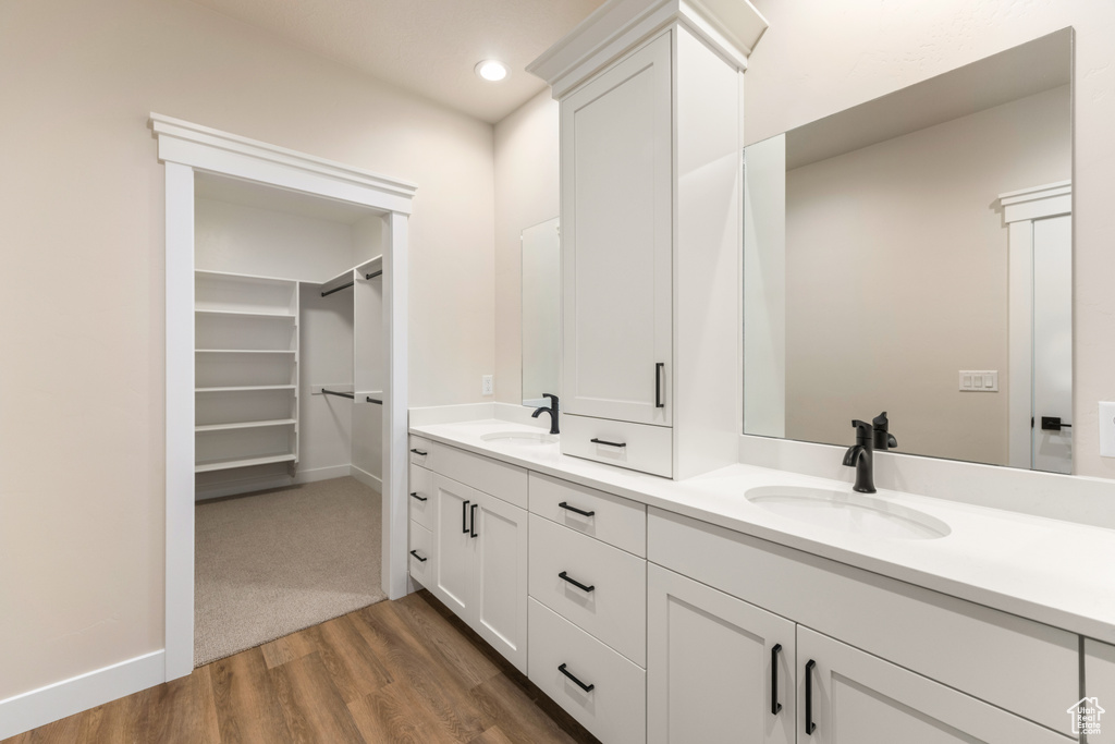 Bathroom with wood finished floors, a spacious closet, double vanity, recessed lighting, and baseboards