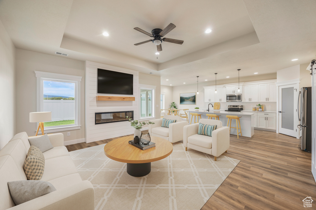 Living room with a tray ceiling, recessed lighting, light wood finished floors, a ceiling fan, and a fireplace